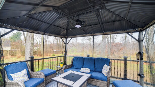 A covered outdoor seating area with wicker furniture and a table, overlooking a garden. - Indiana Dunes Home w/ Gas Grill: 1 Mi to Beach! (Michigan City)