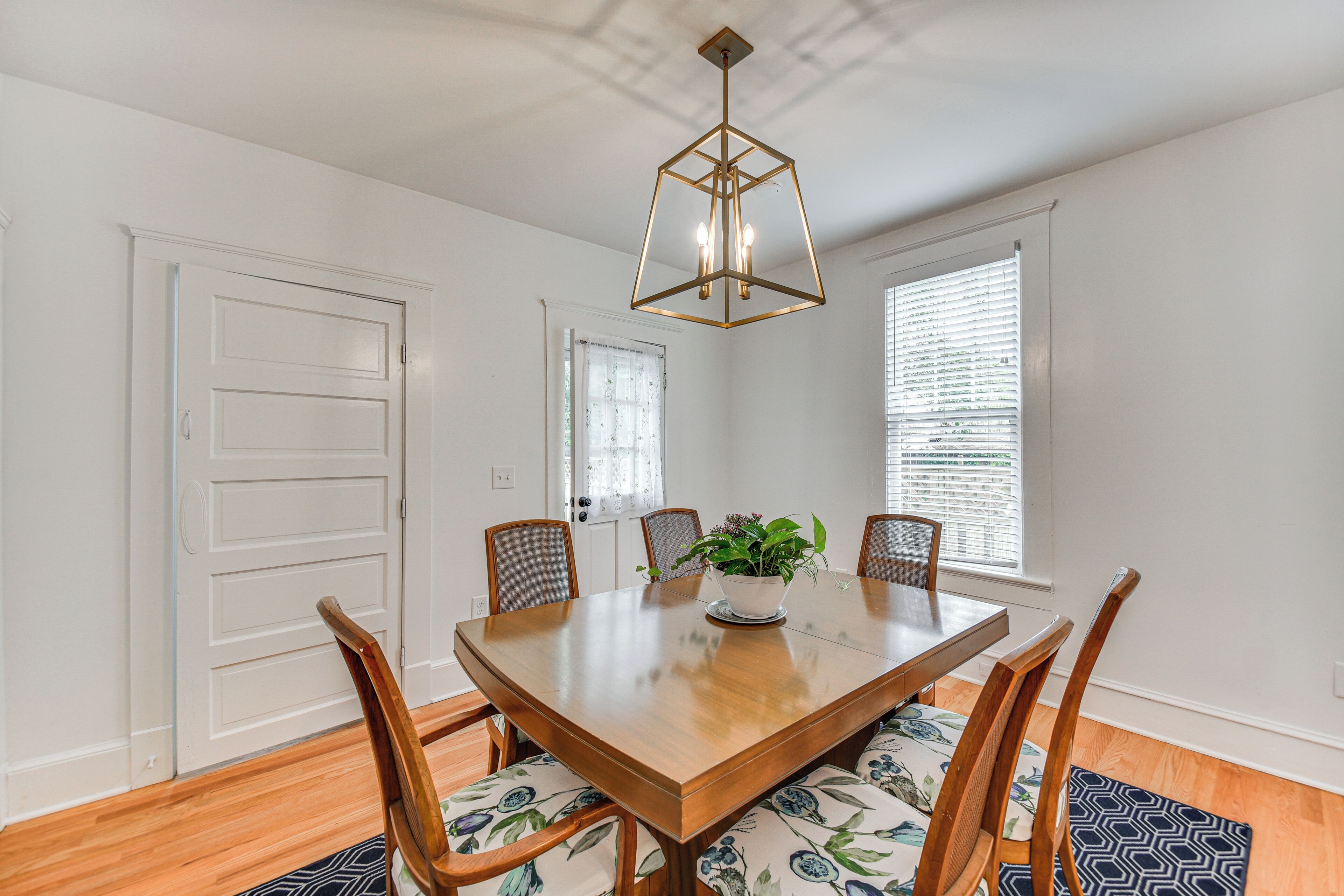 A dining area with a wooden table, six chairs, a potted plant, and a geometric ceiling light fixture.