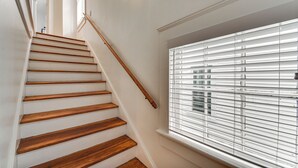 A staircase with wooden steps and a handrail, leading to a room with a window with blinds.