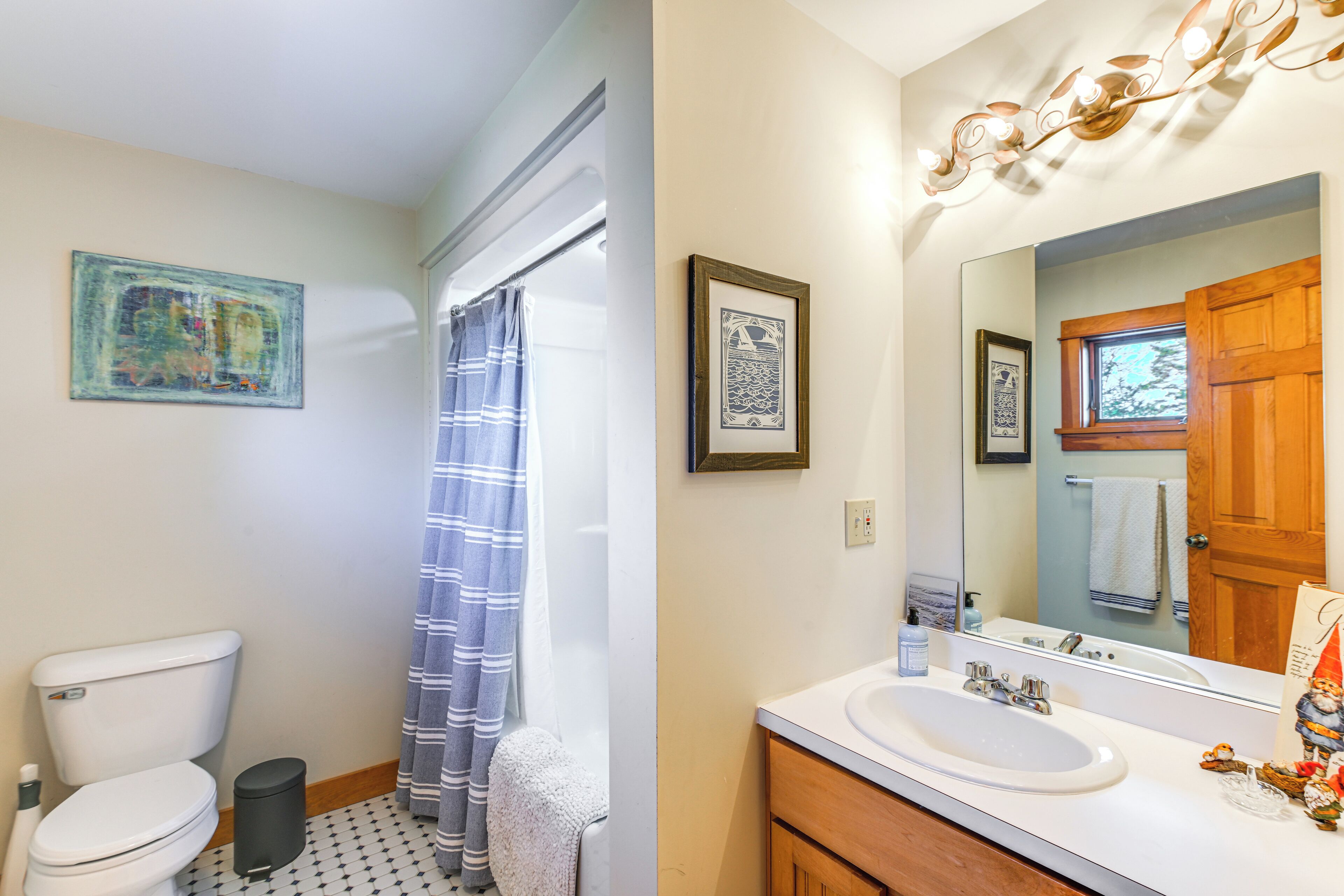 A bathroom with a toilet, a shower with a striped curtain, a sink with a mirror, and a wooden door.