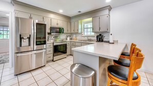 A modern kitchen with stainless steel appliances, a central island, and wooden chairs. - Perry Family Home on 2 Acres w/ Private Pool (Perry)
