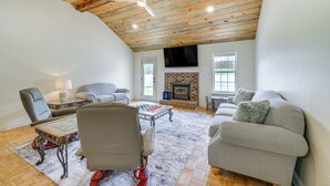 A spacious living room with a high ceiling, a fireplace, and a large window. - Perry Family Home on 2 Acres w/ Private Pool (Perry)