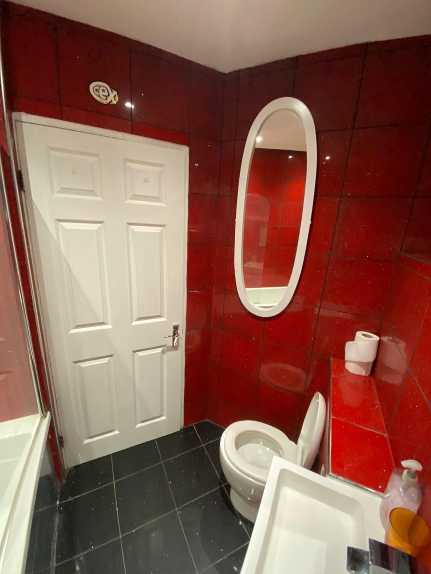 A bathroom with a red tiled wall, a white door, a toilet, and a mirror.