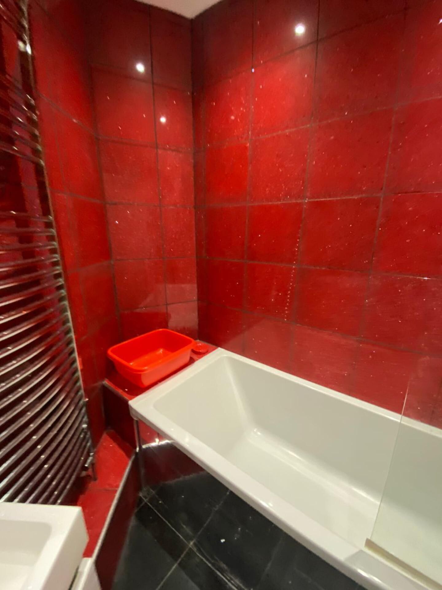 A bathroom with red tiles, a white bathtub, and a red basin.
