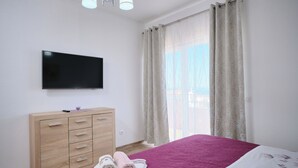 Een slaapkamer met een bed, een aan de muur bevestigde televisie, een houten dressoir en een raam met gordijnen.