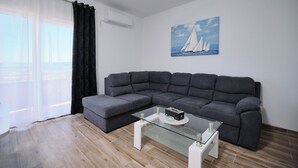 Een moderne woonkamer met een grijze modulaire bank, een glazen salontafel en een schilderij van zeilboten aan de muur.