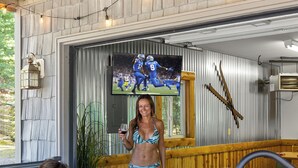 A man relaxing in a hot tub with a woman standing nearby holding a glass of wine. - The Treehouse @ Higgins Lake-HOT TUB- Fireplace-Pets❤️-3 min walk to the lake (Roscommon)