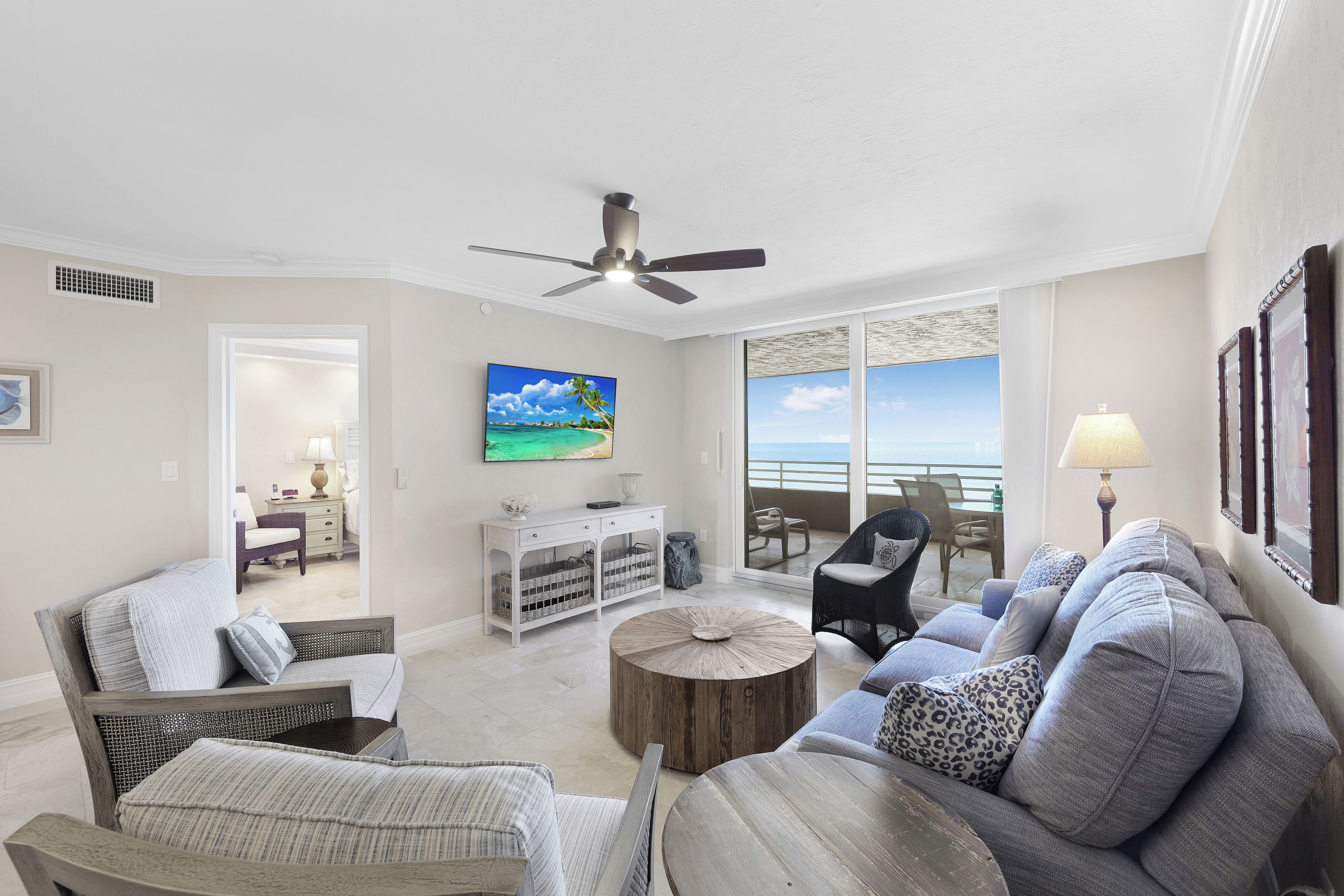 A spacious living room with a large window, a ceiling fan, and a view of the ocean.