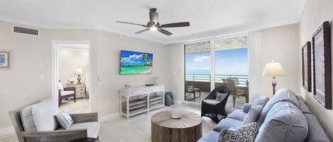 A spacious living room with a large window, a ceiling fan, and a view of the ocean.