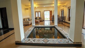 A spacious living area with a central water feature, a seating area with sofas, and a dining area with chairs. - This is a 7-room Lakeside villa with a beautiful view and lawn.  (Kochi)