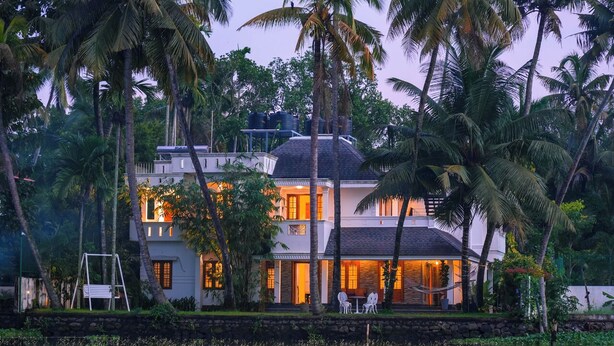 A two-story house with a water body in front, surrounded by palm trees. - This is a 7-room Lakeside villa with a beautiful view and lawn.  (Kochi)