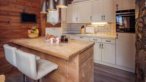 A kitchen with wooden walls, white cabinets, a central island with seating, and a stone accent wall. - Meribel Les Allues Ski Chalet With Beautiful Views Of The Mountains (Les Allues)