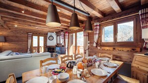 A wooden cabin interior with a dining table set for breakfast, wooden beams on the ceiling, and a window overlooking a snowy landscape. - Meribel Les Allues Ski Chalet With Beautiful Views Of The Mountains (Les Allues)