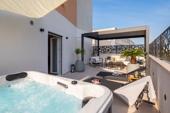 A rooftop terrace with a hot tub, outdoor seating, and a covered area with a decorative fence.
