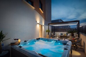 A hot tub with a wooden deck, outdoor seating, and a pergola.