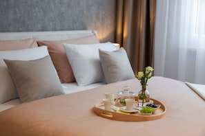 Una cama bien hecha con una bandeja de desayuno que incluye tazas, un tarro de cristal y un florero con flores.