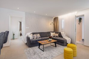 Uma sala de estar moderna com um sofá modular cinza, uma mesa de centro de madeira e pufes amarelos.