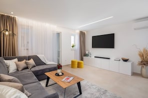 Una sala de estar moderna con un sofá, una mesa de centro, un televisor montado en la pared y un mueble blanco.