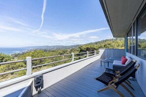 Uma varanda com vista para o mar e colinas, equipada com duas cadeiras de descanso e uma mesa pequena.
