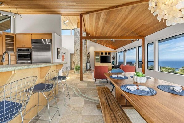 Una cocina moderna con electrodomésticos de acero inoxidable, un comedor con mesa y sillas de madera y vistas al océano.