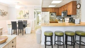 Una cocina moderna con armarios de madera, una isla central con taburetes, un comedor con sillas y un cubo de basura.