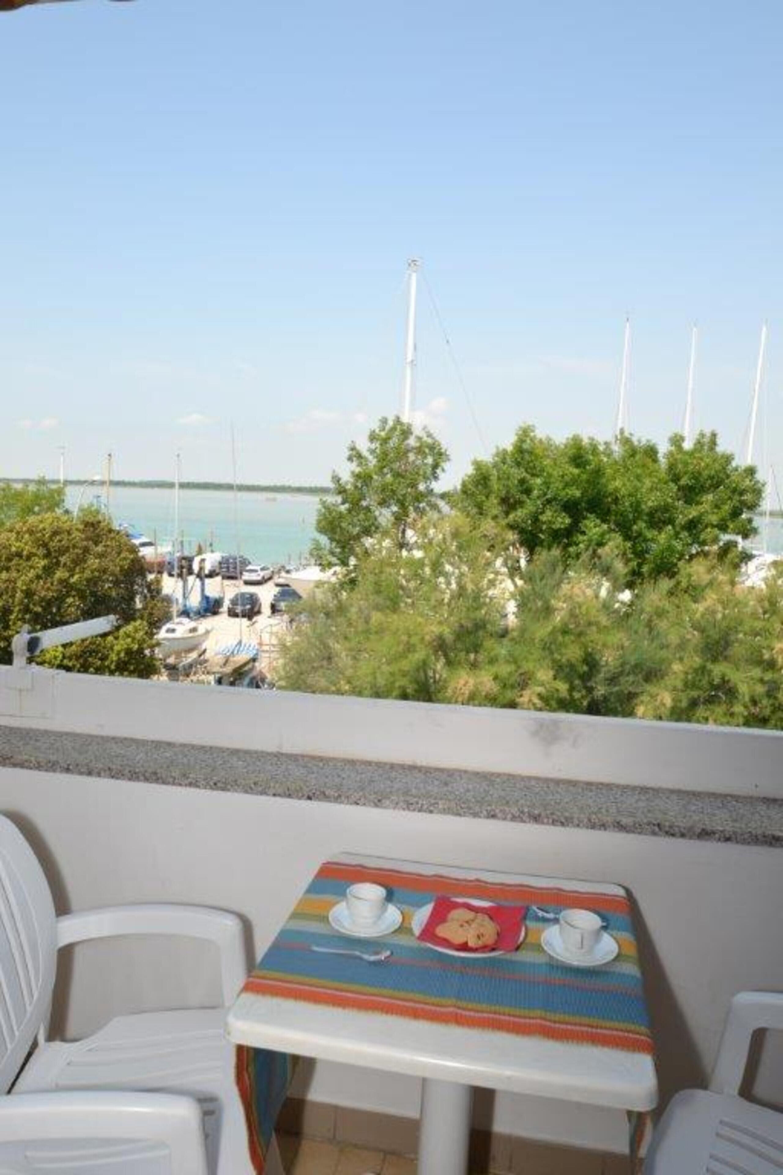 Ein Balkon mit Tisch und Stühlen mit Blick auf einen Hafen voller Boote und einem klaren Himmel.