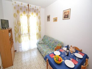 Un comedor con una mesa dispuesta para dos personas, un televisor sobre un mueble bajo y un sofá.