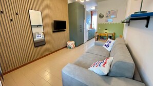 A modern living room with a sofa, a television, and a kitchen area in the background. - Adorable studio with shared pool (Porto Santa Margherita)