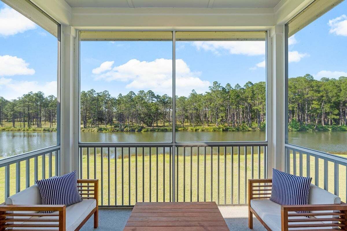 A covered balcony with two wooden chairs and a table, overlooking a lake and forest.