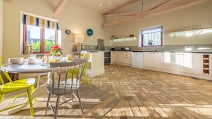 A kitchen with a herringbone floor, wooden beams, a dining area with yellow chairs, and a window with a striped blind. - Harnser Barn, Tittleshall, Norfolk (Tittleshall)