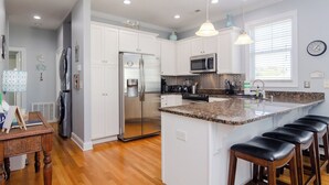 Una cocina moderna con armarios blancos, electrodomésticos de acero inoxidable, encimera de granito y una zona con taburetes de bar.