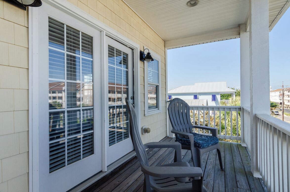 A covered porch with two Adirondack chairs and a door with a window.