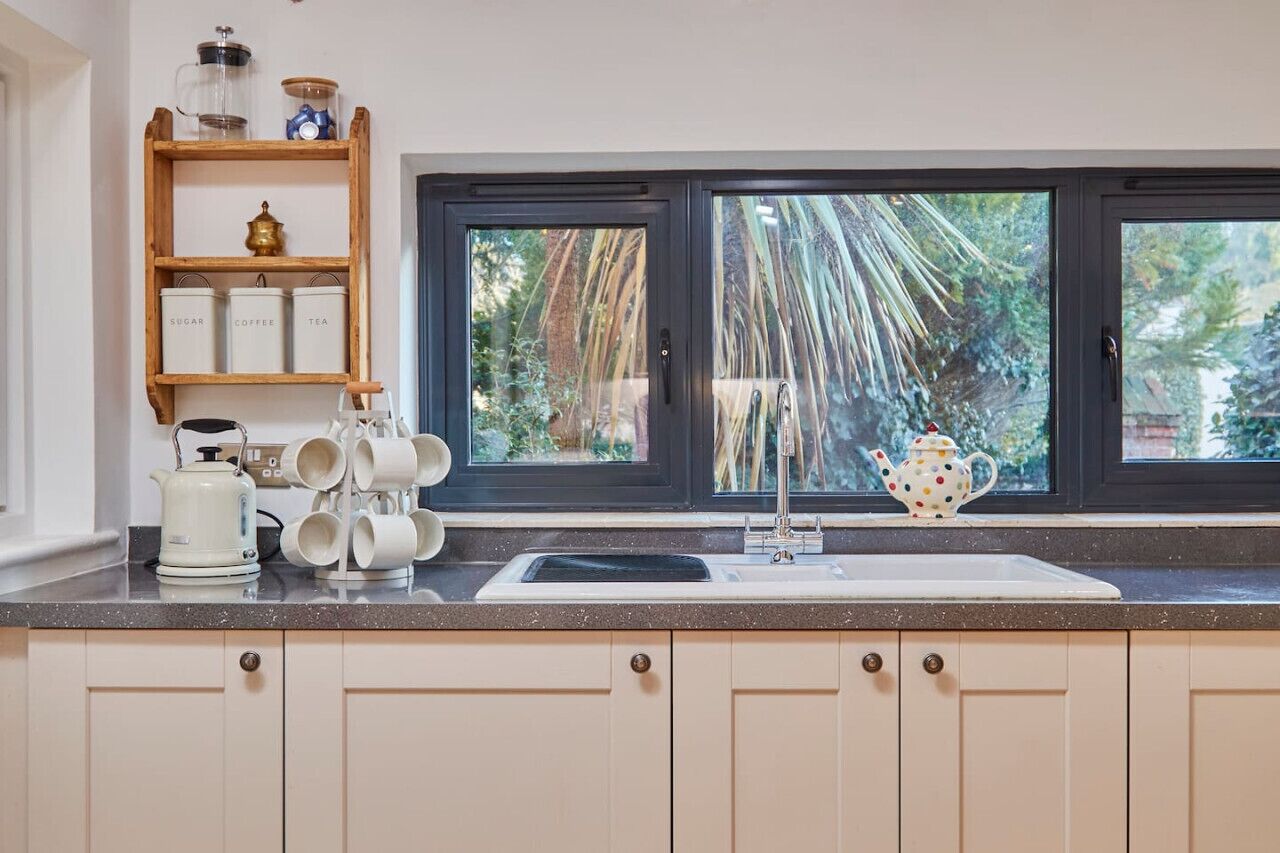Una cocina con ventana, repisas con frascos, un hervidor y una tetera de lunares.