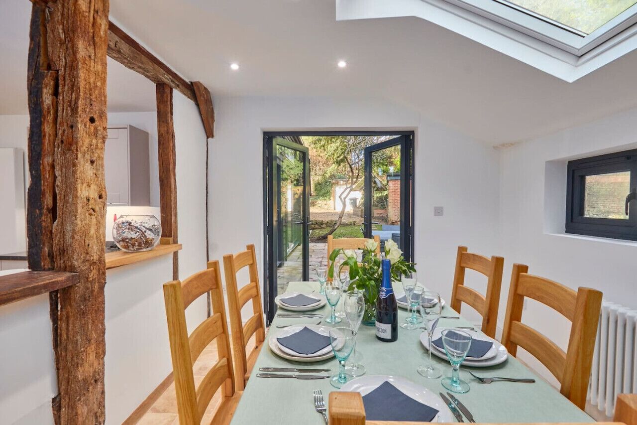 Un comedor con una mesa preparada para seis, sillas de madera, una mesa con cubierta de vidrio y vistas a un jardín exterior a través de un ventanal.