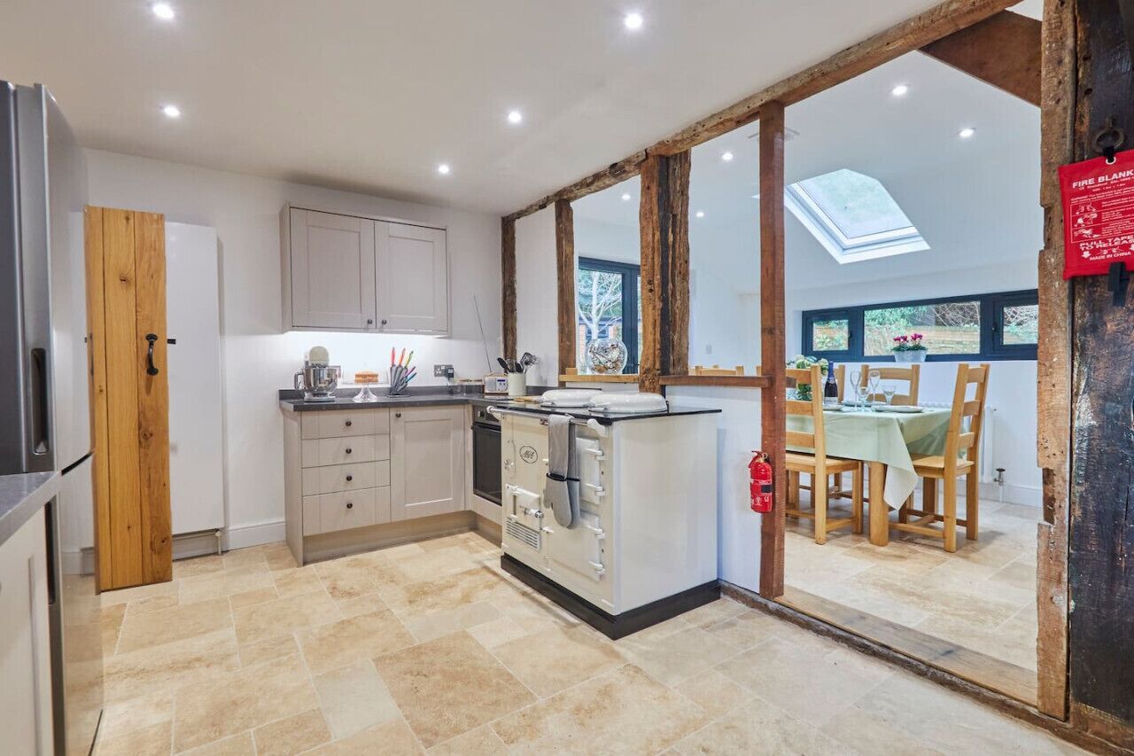 A modern kitchen with a central island, wooden beams, and a dining area with a view.