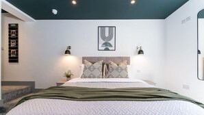 Een moderne slaapkamer met een groot bed, een hoofdbord, twee bedlampen en een gekaderd kunstwerk aan de muur.