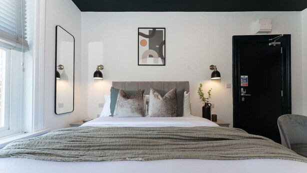 A modern bedroom with a bed, bedside lamps, a wall-mounted abstract art piece, and a door. - Sleek City Stay; Long Stay Discount, FREE Parking (Southampton)