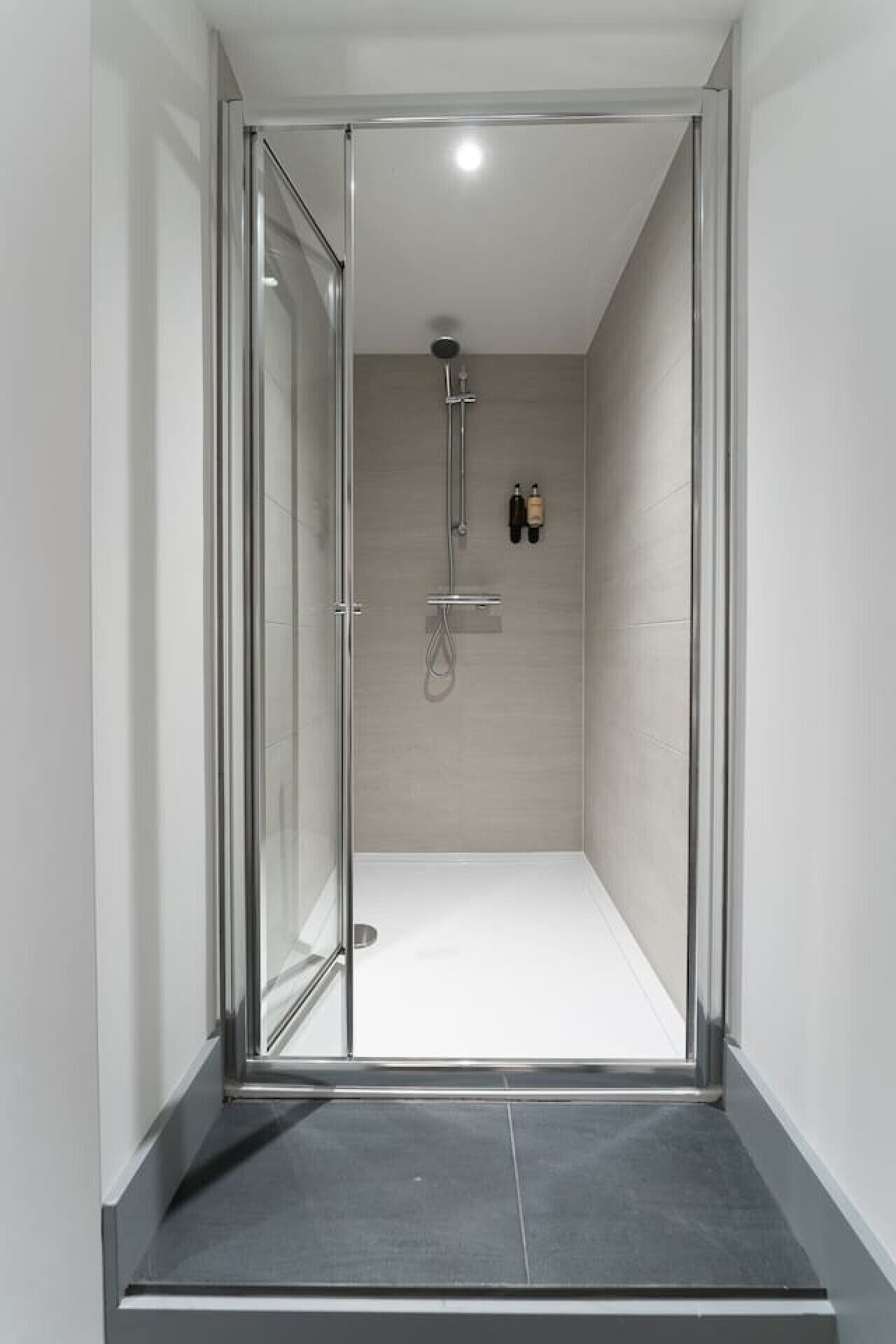 Een moderne badkamer met een glazen douchedeur, een handdouche en een wandmengkraan.