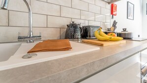Una cocina moderna con un grifo de acero inoxidable, un lavamanos blanco y una encimera con tabla de cortar y plátanos.