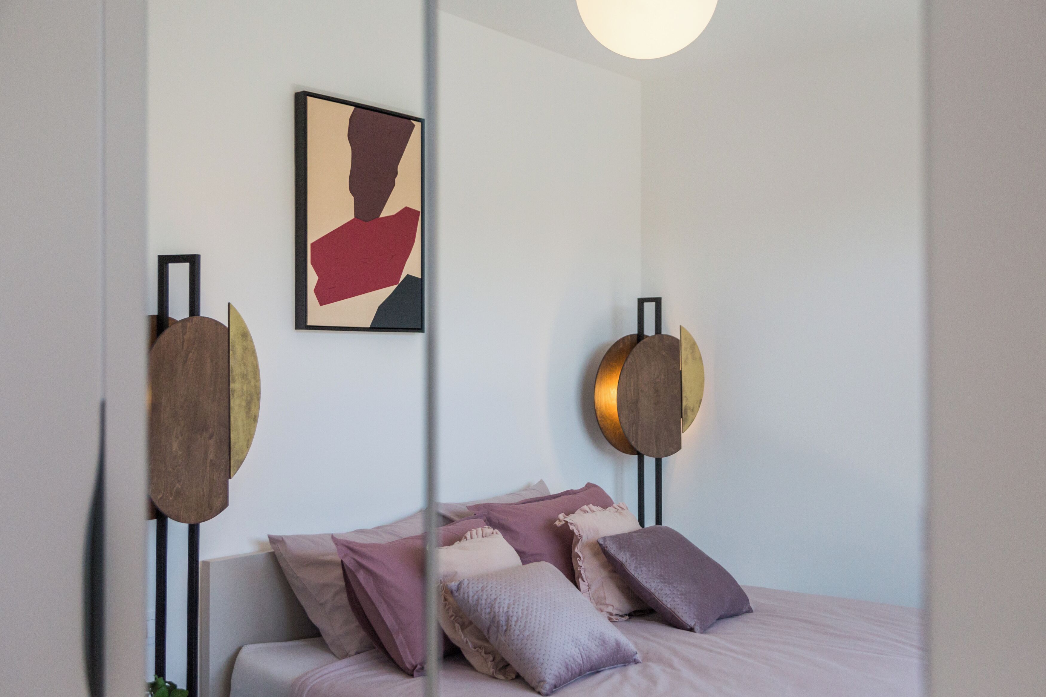 A modern bedroom with a bed, pillows, and a wall-mounted abstract painting.