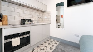 Une cuisine compacte avec des meubles blancs, un four encastré, un four à micro-ondes et un plan de travail agrémenté d’un bloc à couteaux et d’autres ustensiles.