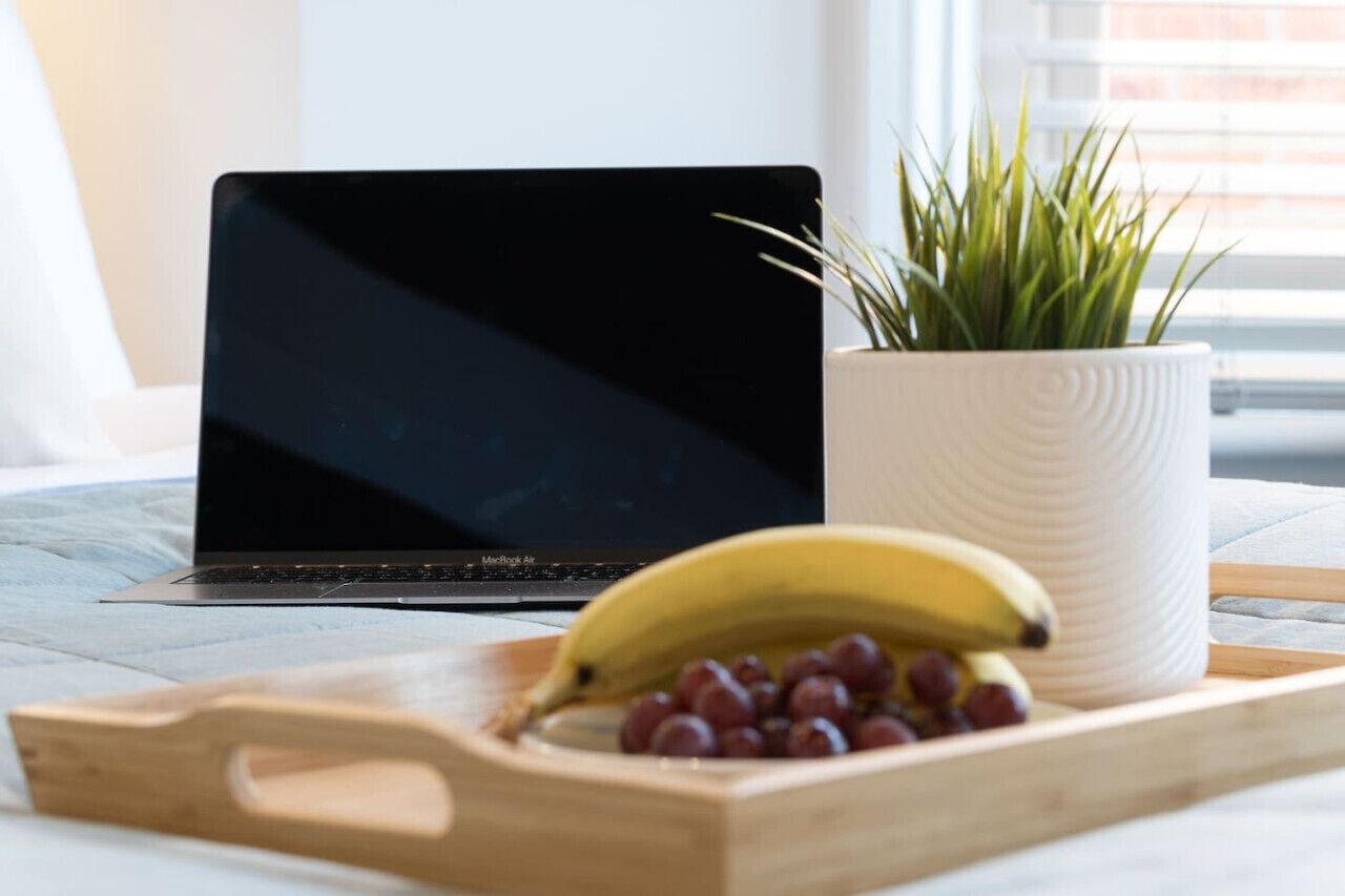 Un ordinateur portable posé sur un plateau en bois, avec une banane et des raisins.