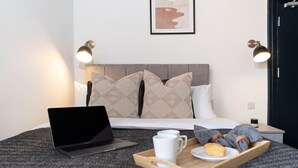 A neatly made bed with a laptop, a tray with a cup and a pastry, and two wall-mounted lamps. - Modern Studio; Long Stay Discounts & Free Parking (Southampton)