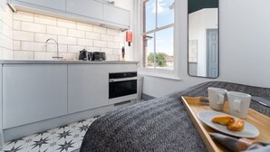 A compact kitchen with white cabinets, a black oven, and a window providing a view of the outside. - Modern Studio; Long Stay Discounts & Free Parking (Southampton)