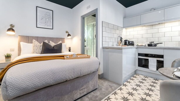 A modern bedroom with a large bed, a small kitchenette, and a bathroom visible through an open door. - Modern Studio; Free Laundry & Parking, Fast WIFI (Southampton)