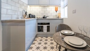 A compact kitchen with white tiles, a stove, oven, and a dining area with a table set for two. - Modern Studio; Free Laundry & Parking, Fast WIFI (Southampton)