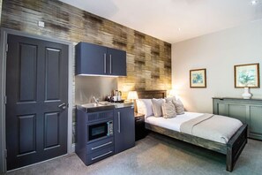 A compact bedroom with a bed, a small kitchenette, and a door.