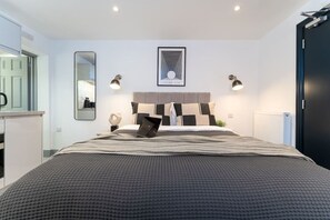 Ein modernes Schlafzimmer mit einem großen Bett, einem Kopfteil mit geometrischem Muster, zwei Wandlampen und einem gerahmten Bild über dem Bett.