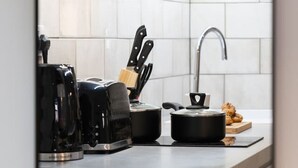 Ett modernt kök med vita kakelplattor, en inbyggd ugn, en kaffemaskin och ett knivställ.
