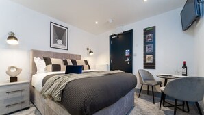 Ett modernt hotellrum med en stor säng, sängbord, ett skrivbord med två stolar, en TV och en dörr med en skylt.